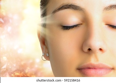 Extreme Close up face shot of young woman with eyes closed.Girl doing mental exercise against bright background with light beam.