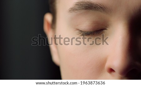 Extreme close up of half face shot of serious female face indoors. Macro of tired woman eye looking straight at camera on black background.Sleepy girl closing eyes.