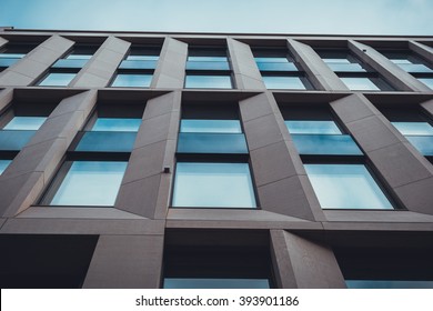 Extreme Close Up And Low Angle View Of Modern Commerical Low Rise Office Building With Windows And Brown Stone Pillars Against Hazy Blue Sky - Abstract Architectural Background