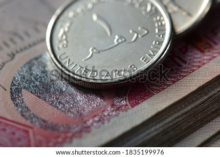 Extreme close up of one Dirham coin placed over hundred dirham note. Currency and coins of UAE.