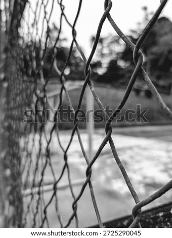 Extreme close up perspective emphasizes the intricate woven texture of a rusted chain link fence in monochrome, suggesting themes of boundary separation and protection beyond the blurry field.