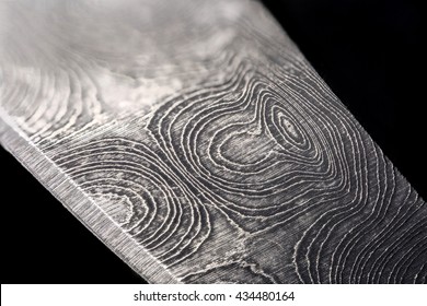 Extreme close up of the raindrop patterning on a damascus steel knife blade, isolated on black.