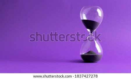 Extreme close up of a transparent hourglass with flowing black sand on blur pink background. Old classic timer. Time concept