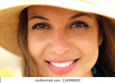 Extreme close up of young model face with straw hat smiling at camera under summer rays sun on the beach. Very close up of photogenic model for tanning or cosmetics cream.