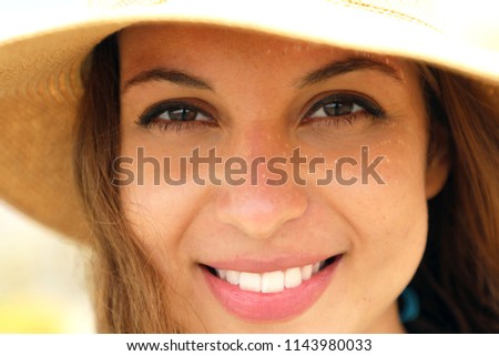Extreme close up of young model face with straw hat smiling at camera under summer rays sun on the beach. Very close up of photogenic model for tanning or cosmetics cream.