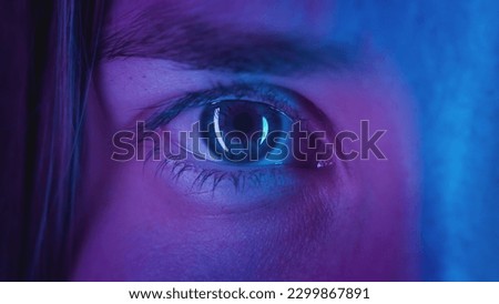 Extreme close-up Beautiful girl opens one eye, neon pink blue light. Attractive feminine look. Party nightclub, fashion show. Macro slow motion. The woman plays video games. Urban eyesight concept.