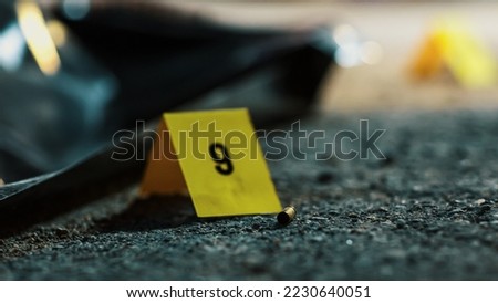 Extreme Close-up: Bullet Shell Found Near the Corpse of The Victim Suggests Gun as Murder Weapon. Mass Shooting Resulting in Tragic Death of Many Innocent Civilians. Forensics Marking Evidence