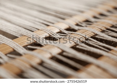 Extreme close-up of interlaced threads crossing over a wooden loom, showcasing fine fiber texture and weaving pattern with shallow depth of field