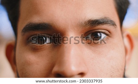 Extreme close-up macro portrait of smiling indian man face. Young guy eyes looking at camera. Adult positive hindu man opening wide his closed eyes. Brown eyes of brunette hispanic male attractive