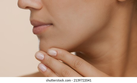 Extreme close-up shot of young woman with perfect skin strokes her jaw line and chin on beige background | Smooth skin and beauty care commercial concept