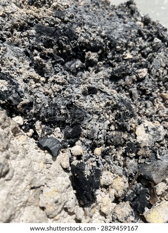 Extreme close-up texture of volcanic ash, charcoal embers, and sulfur mineral deposits on rough geothermal rock ground.