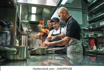 Extreme cooking. Profesional chef teaching his two young trainees how how to flambe food safely. Restaurant kitchen - Powered by Shutterstock