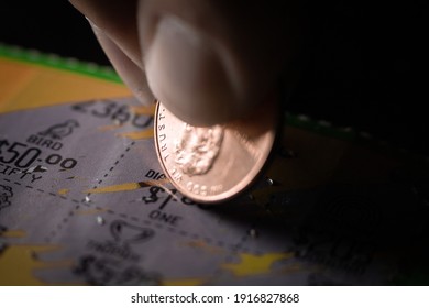 Extreme Macro Close-Up Of A Caucasian Person's Hand Holding A Penny And Scraping A Scratch-Off Lottery Ticket