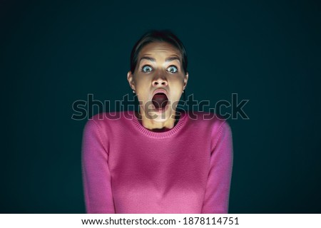 Extreme. Portrait of young crazy scared and shocked caucasian woman isolated on dark background. Copyspace for ad. Bright facial expression, human emotions concept. Looking horror on TV, cinema.