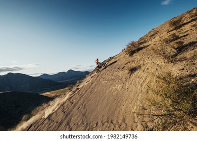 Extreme Rider climbing sand mountain top on off-road cross enduro motorcycle. Beautiful mountains landscape down on background, colourful autumn forest and river in sunshine  - Powered by Shutterstock