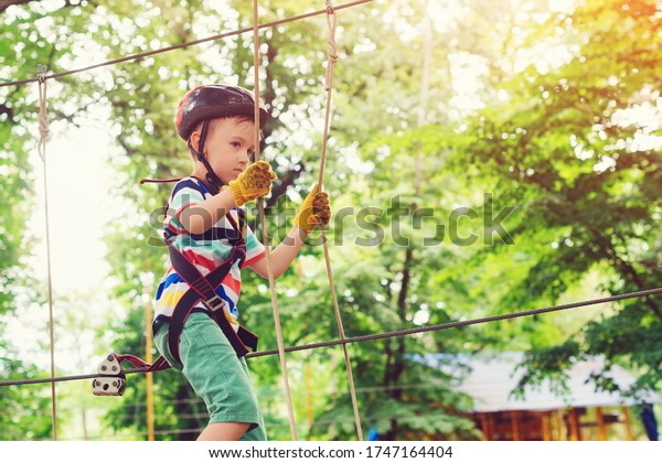 Extreme sport in adventure park.\
Climbing the rope park. Summer camp. The boy climbs a rope park.\
Little cute boy in a climbing adventure park. Summer sunny\
day.