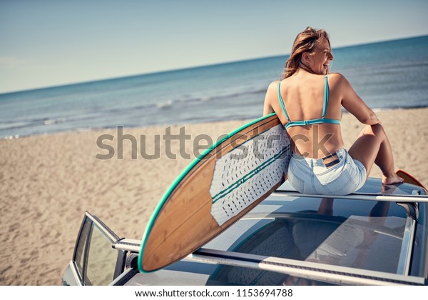 Extreme Sport. Surfing.\
Smiling surfer girl sitting on the car and getting ready for\
surfing. Back view\
