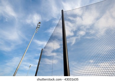 Extreme Wide Angle View Of Backstop Net And Stadium Lights At Baseball Or Softball Playing Field. Angle Is Looking Up Towards The Sky On A Sunny Day.