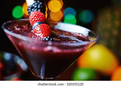 extremely close up glass of tasty tropical alcohol cocktail with berries or lemonade with beautiful decoration on a table in a restaurant with backgrounds of bright colored lights. soft focus.