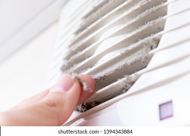 Extremely dirty and dusty white plastic ventilation air grille at home close up and a hand holding dust by fingers, harmful for health.