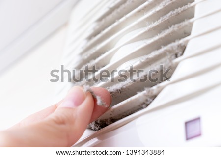 Extremely dirty and dusty white plastic ventilation air grille at home close up and a hand holding dust by fingers, harmful for health.
