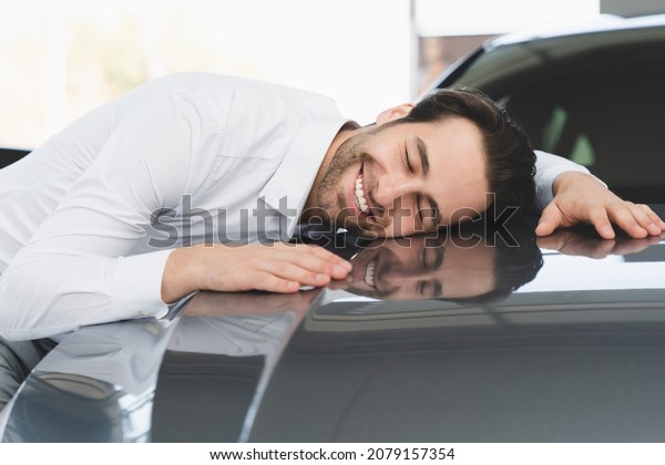 Extremely happy caucasian young businessman\
hugging embracing his new car, feeling excited after buying\
expensive auto at auto dealer shop\
store.