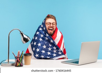 Extremely Happy Funny Man Employee Sitting Wrapped In American Flag And Shouting For Joy In Office Workplace, Celebrating Labor Day Or US Independence Day 4th Of July, Government Employment Support.