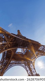 Extremely low angle view of the Eiffel Tower with sparkles and sun glare through the intricate ironwork under a clear blue sunset sky.