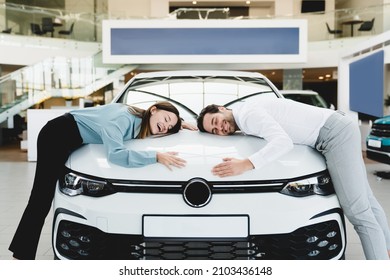 Extremely satisfied happy caucasian young couple family husband and wife hugging embracing their new car, feeling excited after buying expensive auto at auto dealer shop store. - Powered by Shutterstock