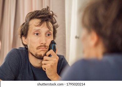 Extremly Tired Young Man Looking At Himself In The Mirror, Home Alone. Self-isolation At Home, Quarantine Due To Pandemic COVID 19. Mental Health Problems In Self-isolation At Home