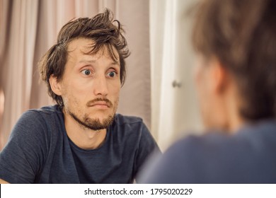 Extremly Tired Young Man Looking At Himself In The Mirror, Home Alone. Self-isolation At Home, Quarantine Due To Pandemic COVID 19. Mental Health Problems In Self-isolation At Home