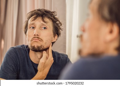 Extremly Tired Young Man Looking At Himself In The Mirror, Home Alone. Self-isolation At Home, Quarantine Due To Pandemic COVID 19. Mental Health Problems In Self-isolation At Home