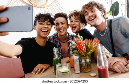 Extrovert friends taking a selfie while sitting together during lunch. Group of young queer people smiling cheerfully in a restaurant. Friends bonding and spending time together.