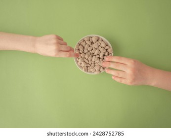 Extruded heart-shaped bran in a white cup on a green background, children's hands reach out to the delicacy from different sides and hold the bran with their fingers. A place for the text. - Powered by Shutterstock