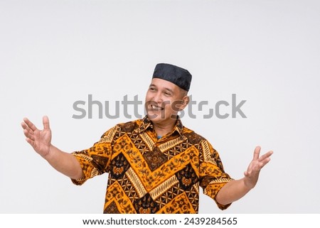 Exuberant Indonesian man in traditional batik shirt and kopiah hat gesturing dramatically, making grandiose claims. Isolated on white background.