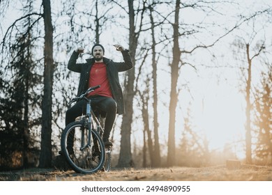 An exuberant man raising arms in triumph while sitting on a mountain bike in a park, against a backdrop of sunset and trees. - Powered by Shutterstock