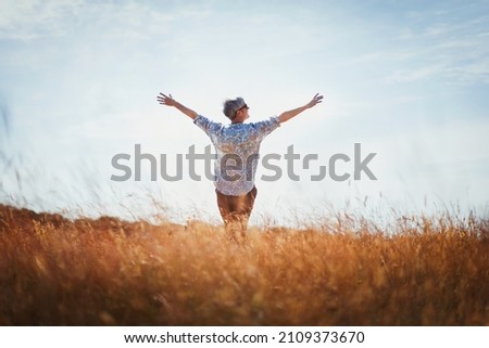 Exuberant senior woman with arms outstretched in sunny field