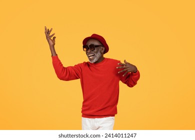 Exuberant smiling senior man in a red sweater and hat, dancing with arms raised, wearing sunglasses, embodying joy and carefree vibes, fun, on a vivid yellow background, studio - Powered by Shutterstock