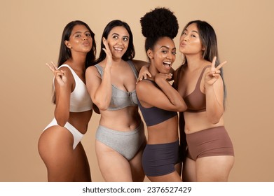 Exuding natural beauty, four multiracial women playfully grimacing, gesturing and posing, sharing joyful, unscripted moment of genuine friendship and unity in the studio