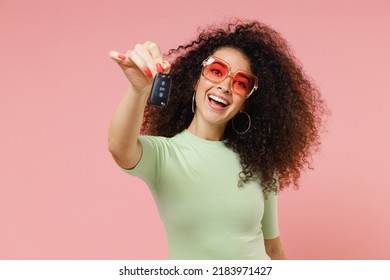 Exultant happy young curly latin woman 20s wears mint t-shirt sunglasses hold give present vehicle key to camera you isolated on plain pastel light pink background studio portrait. Car sales concept - Powered by Shutterstock