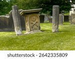 Eyam village Derbyshire UK. The site of the great bubonic plague between 1665 and 1666. Ancient stone grave marker with skull and crossbones in a lush cemetery.