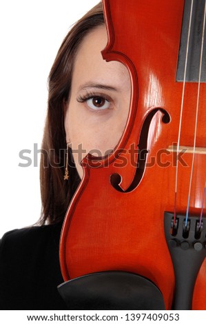 The eye of a beautiful woman hiding behind a violin looking into the
camera in a close up image, isolated for white background
