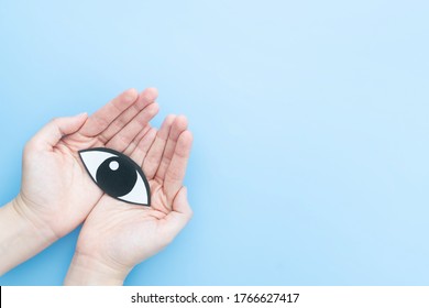 Eye Care, Healthy Vision And Ophthalmology Concept. Human Hand Holding Eyes Shape Made From Paper On Light Blue Background. Copy Space.