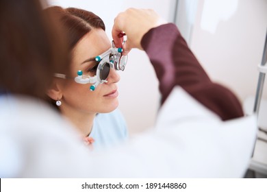 Eye doctor inserting the trial lens in a left eye socket of glasses for testing eyesight - Powered by Shutterstock