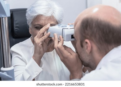 Eye Doctor Using Modern Tool Checking Woman Patient Eyesight In Optical Clinic, Optometrist Man Testing Eye With Senior Indian Woman In Optic Clinic, Expert Optician Doing Eye Exam For Elderly Woman