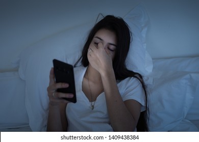 Eye Fatigue Due To Blue Light From Smartphone Screen. Millennial Young Sleepy Girl Using Mobile Phone In Bed At Night. Cellphone Addition And Tech Sleep Disorders Concept.