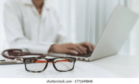 Eye Glasses On Desk With Blur Background Of Doctor With Laptop ,working In Hospital Office