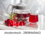 Eye level shot of red cherry herbal tea in a glass teapot and cup served with a bunch of fresh ripe cherries on a sunlit table
