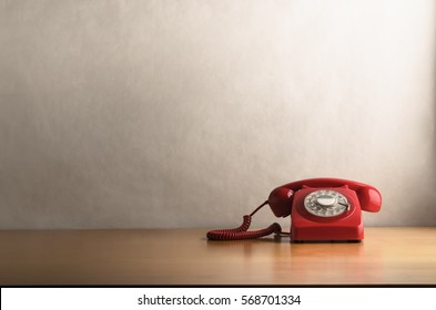 Eye level shot of a retro red telephone (British circa 1960s to 1970s) on a light wood veneer desk or table with off white background providing copy space.
