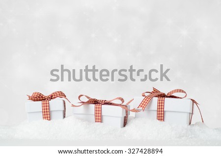 Eye level shot of three white Christmas gift boxes with lids, in a row and bow tied with gingham checked ribbons, nestling in artificial snow with sparkly star bokeh background.